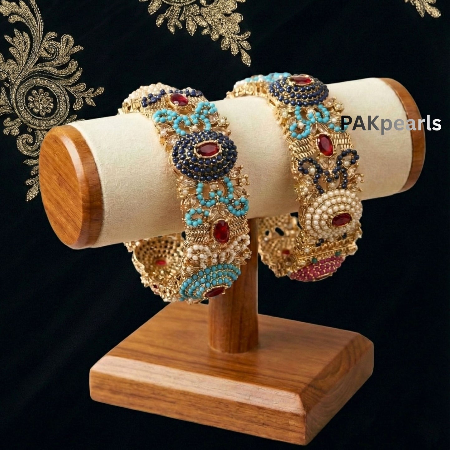 Close-up of a pair of gold Nauratan openable bangles featuring turquoise, red, and dark blue gems with pearl accents on a wrist.