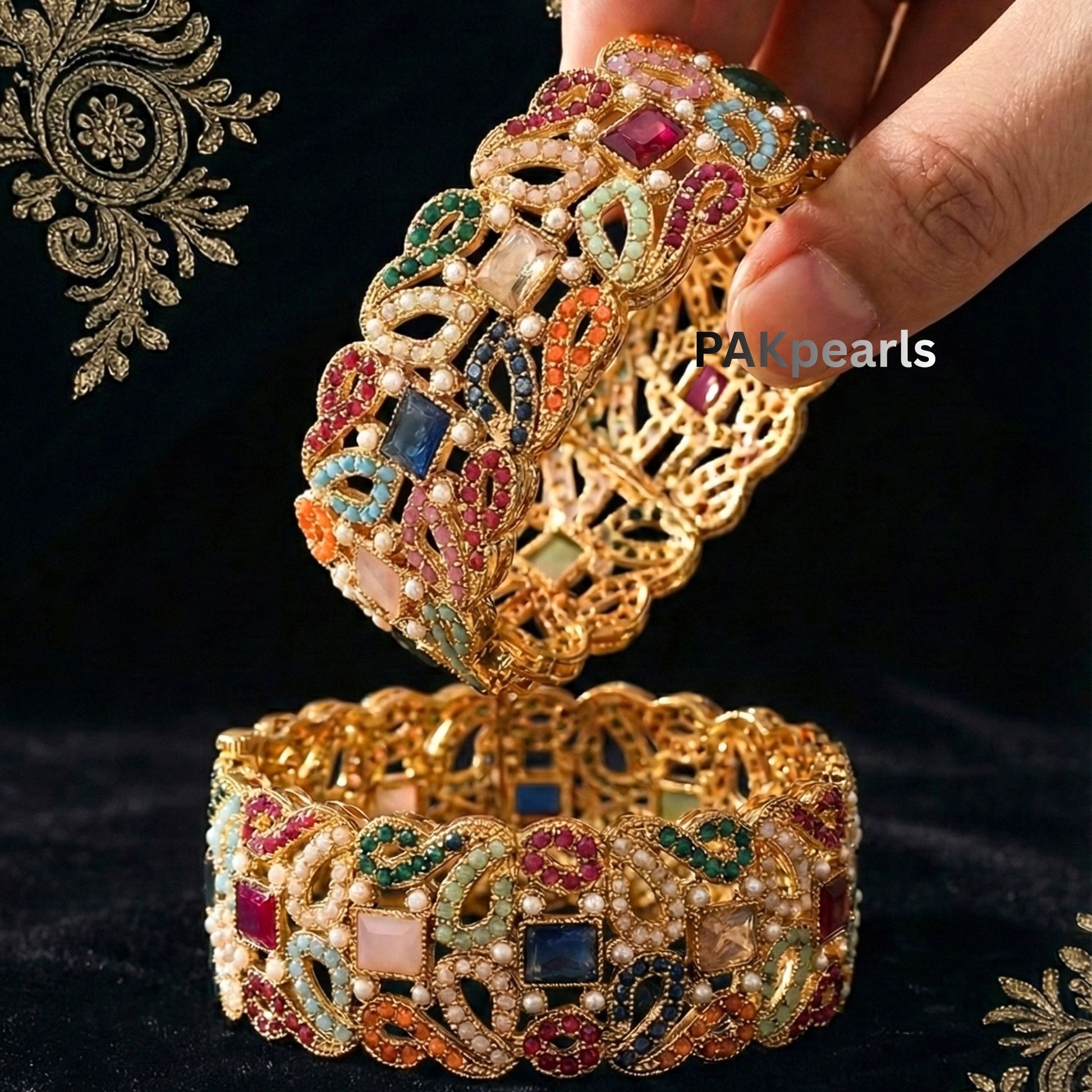 Pair of wide Nauratan gold-plated bangles featuring multi-colored stones and pearl accents displayed on a wooden stand.