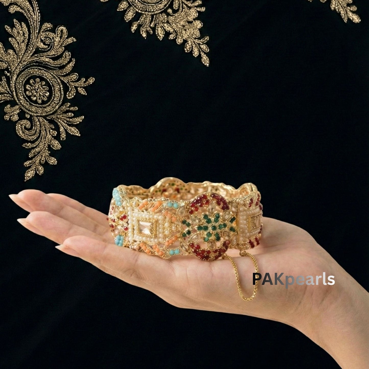 Hand wearing heavy gold Nauratan bangles from PAKpearls, showcasing the detailed craftsmanship and vibrant stone setting.