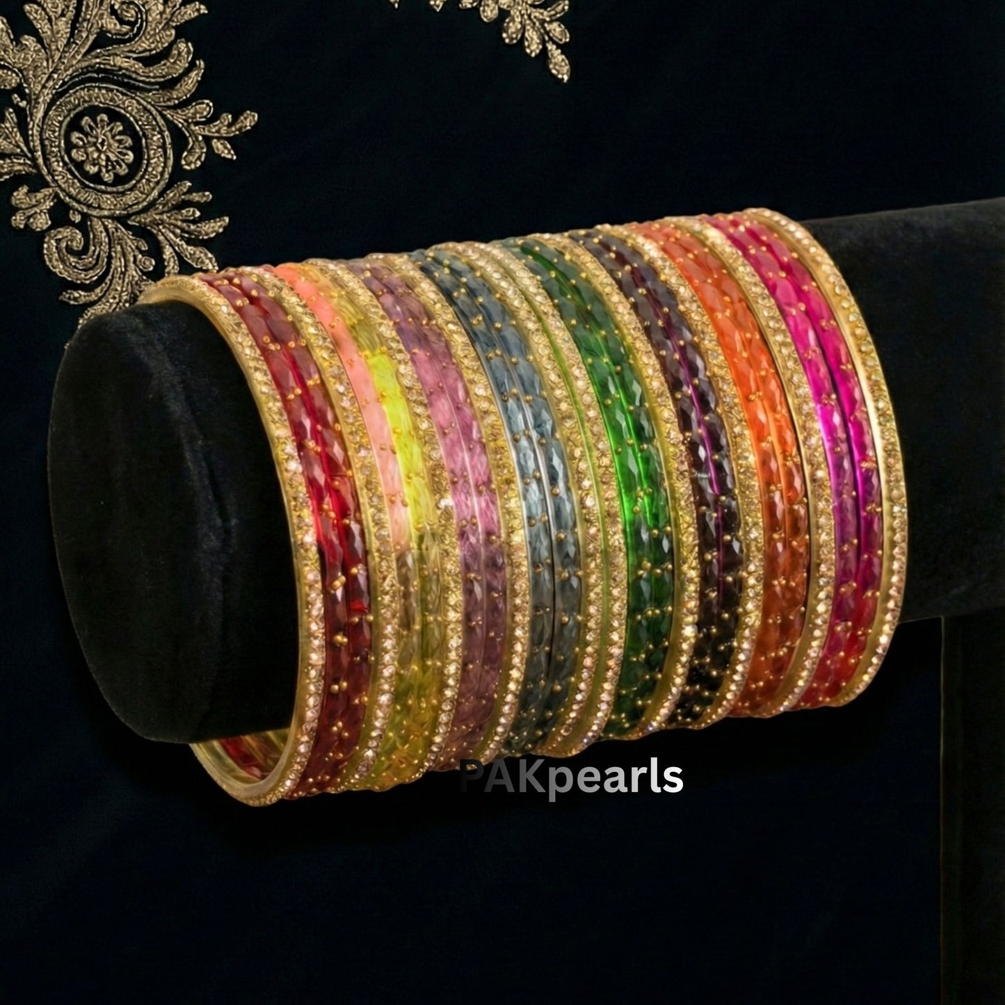 Detailed shot of textured "Raindrop" faceted glass bangles in rainbow colors including emerald green, ruby red, and magenta with sparkling gold accents.