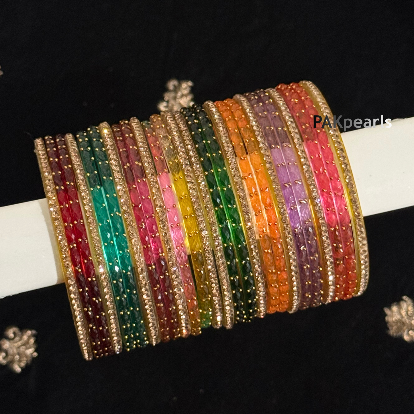 Close-up of light-reflecting faceted glass bangles in a spectrum of colors, showcasing the "Raindrop" sparkle and gold metallic trim.